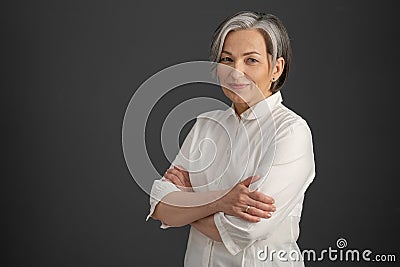 Intelligent silver-haired woman smiles with arms crossed. Pretty business woman looking at camera confidently. Stock Photo
