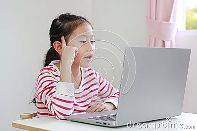 Intend asian little child sitting at desk and using laptop at home Stock Photo