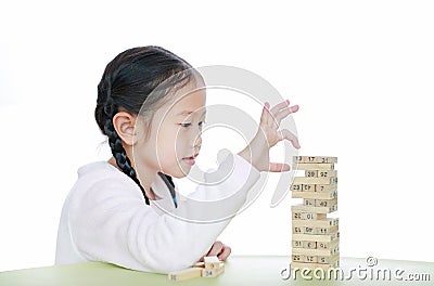 Intend little Asian child girl thinking to playing wood blocks tower game for Brain and Physical development skill in a classroom Stock Photo