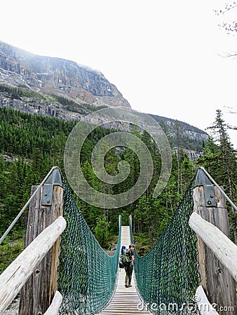 An interesting view of a female hiker looking back as she crosses a suspension bridge high in the remote forests of the rockies Stock Photo