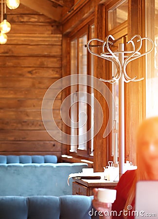 The interior of a cozy cafe with wooden tables, walls, comfortable blue sofas, a hanger. Morning. Sunny. Female freelancer connect Editorial Stock Photo