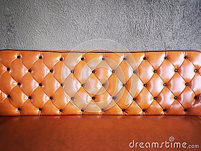 Vintage orange or brick colour leather sofa with grey concrete wall background. Stock Photo