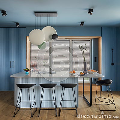 Interior design of kitchen space with marble island, black chockers, modern lamp, wooden wall, blue kitchen furnitures, vase with Stock Photo