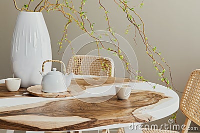 Interior design of stylish dining room interior with family wooden and epoxy table, rattan chairs, flowers in vase and teapot. Stock Photo