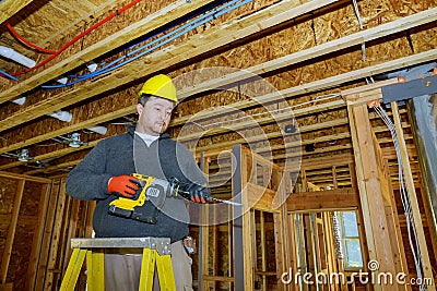 Interior frame of a new house under construction worker drills hole with wooden ceiling the electrical wiring Stock Photo