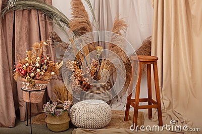 Interior of house is decor in brown tones: wooden chair, knitted pouf, wicker baskets, vases with dried flowers and pampas grass. Stock Photo