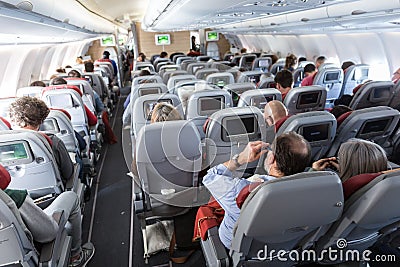 Interior of large commercial airplane with passengers on their seats during flight. Editorial Stock Photo