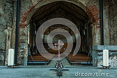 Interior of a medieval ruined church with altar cross and candles and the prayer benches Stock Photo