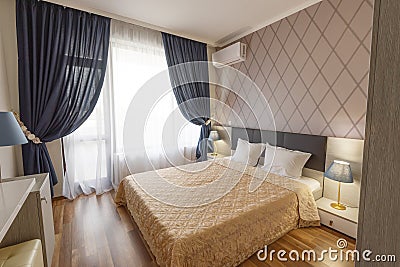 Interior of modern bedroom with cozy double bed. Windows with long curtains, drapery and sheers. Interior photography Stock Photo