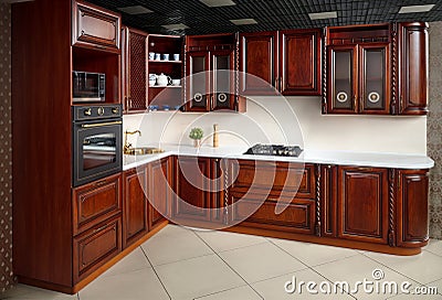 Interior of modern kitchen in classic style with golden elements cherry alder wood cabinetry with built-in appliances electric or Stock Photo