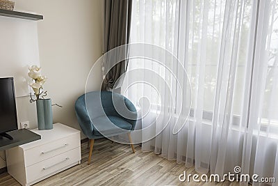 Interior of modern room with comfortable armchair near to large window with sheers and gray curtains Stock Photo