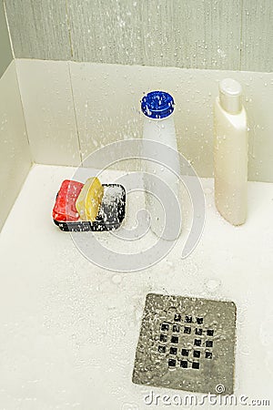 Interior of a shower cabin with bottles of shampoo and conditioner next to bars of soap with the water from the shower head Stock Photo