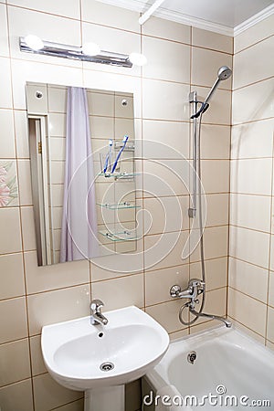 Interior of simple half bathroom with sink with mirror and bath with shower, white sanitary ware Stock Photo