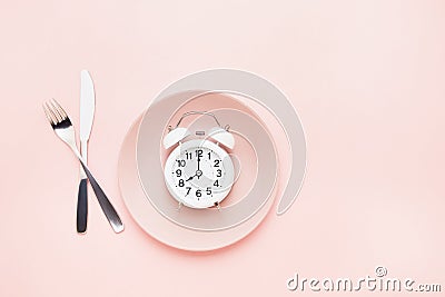 Intermittent fasting concept. White alarm clock on empty pink dish with knife and fork on pink background. top view, copy space Stock Photo