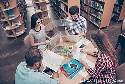 International group of four focused clever young students bookworms studying in the college library, sit and doing assignments Stock Photo