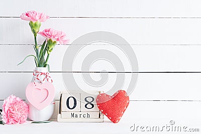 International Womens day concept. Pink carnation flower in vase and red heart with March 8 text on wooden block calendar on white Stock Photo