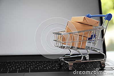 Internet shopping. Small cart with boxes on modern laptop, space for text Stock Photo