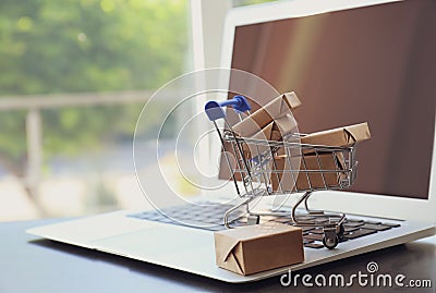 Internet shopping. Small cart with boxes and modern laptop on table indoors, space for text Stock Photo