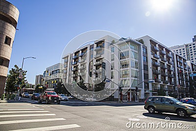 An intersection at Grand Ave and Olympic Blvd with a white and brown apartment building, cars driving and people walking Editorial Stock Photo