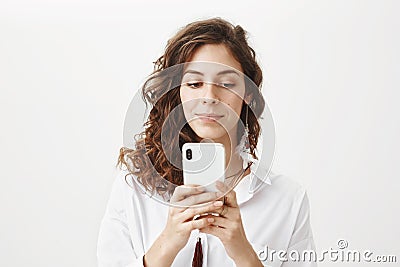 Intrigued and positive sensual caucasian woman with curly hair holding smartphone while messaging or playing games Stock Photo