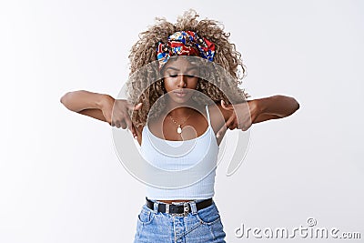 Intrigued and thoughtful, serious-looking blond curly-haired hipster woman with stylish headband, bend, pointing and Stock Photo