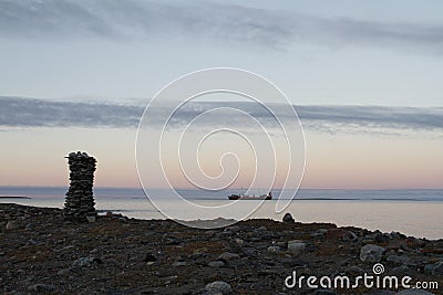 Inuksuk along arctic shore with barge in background Stock Photo