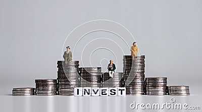 INVEST word written in white cube. Pile of coins in the shape of a graph. Miniature people. Stock Photo