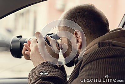 Investigator or private detective or reporter or paparazzi sitting in car and taking photo with professional camera Stock Photo