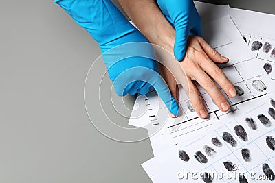 Investigator taking fingerprints of suspect on grey table, closeup. Stock Photo