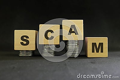 Investment scam, fraud and Ponzi scheme concept. Stack of coins on wooden blocks with word fraudulent in dark black background. Stock Photo