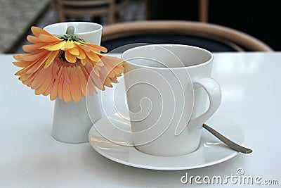 Inviting scene with simple white coffee cup and saucer, single flower as a welcome to morning Stock Photo