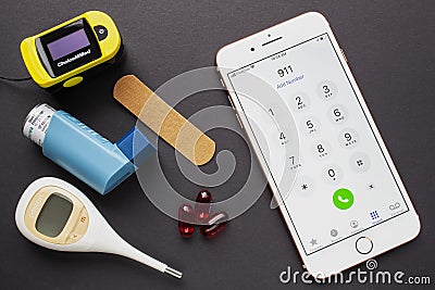 An iPhone with the 911 dial emergency services, with an asthma inhaler, a bandage, some pills, and an oximeter on a black Editorial Stock Photo