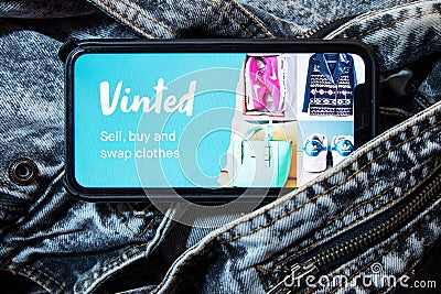 Iphone with vinted logo on screen with hand on vintage denim fabric background. Editorial Stock Photo