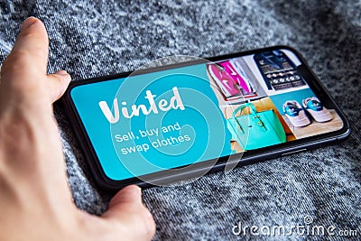 Iphone with vinted logo on screen with hand on vintage denim fabric background. Editorial Stock Photo