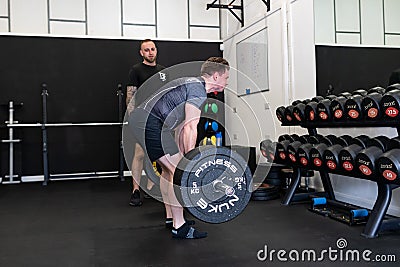 Ipswich Suffolk UK April 03 2022: Muscular young man working out with a barbell in a small gym being coached by a personal trainer Editorial Stock Photo