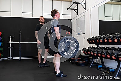 Ipswich Suffolk UK April 03 2022: Muscular young man working out with a barbell in a small gym being coached by a personal trainer Editorial Stock Photo