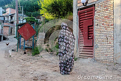 Mazandaran, Iran - 19 July 2017: Iranian woman with traditional colourful burka in a rural area of Iran walking in the village Editorial Stock Photo