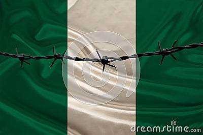 Iron barbed wire against the background of the national silk flag of the state of Nigeria, concept of imprisonment for offenders, Stock Photo