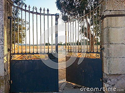 Iron gate with a small opening to let a person with visible narrow path through the opening. Stock Photo