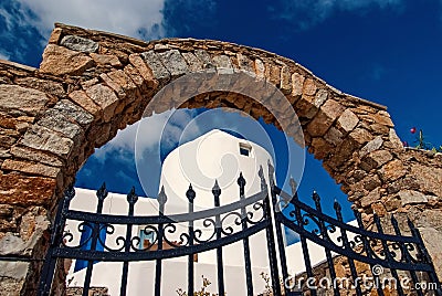 Iron gate and stone arch in Mykonos, Greece. Archway structure or architecture. Whitewashed building on sunny outdoor Stock Photo