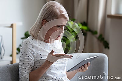 Irritated aged woman holding broken tablet having problems with gadget Stock Photo