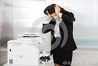 Irritated Businesswoman Looking At Paper Stuck In Printer Stock Photo