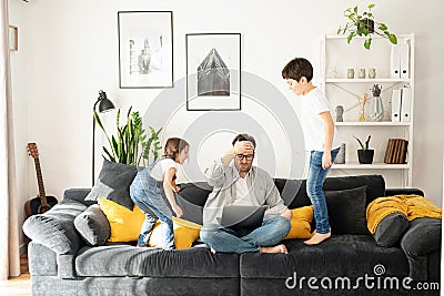 Irritated freelancer parent is babysitting and working. Annoyed father sitting with laptop with eyes closed, covering Stock Photo