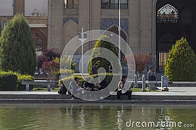 A group of young Iranians resting near a fountain in the Imam Square. Ali Qapu Palace on the background Editorial Stock Photo