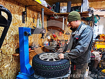 Ishim, Russia - November 27, 2023: A mechanic repairs a car wheel and makes a tire in a dirty garage. Replacement of Editorial Stock Photo