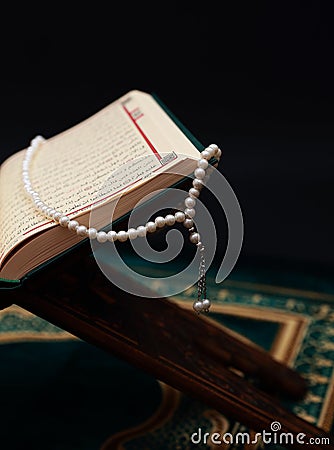 Islamic Holy Book Quran on wood carving rahle with rosary beads and prayer rug on black background. Kuran the holy book of Muslims Editorial Stock Photo