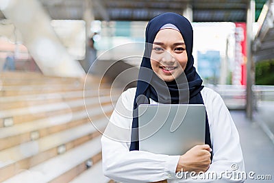 Islamic student or working woman standing with her arms crossed holding her laptop, smiling confidently Stock Photo