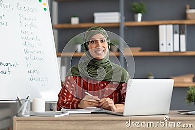 Islamic teacher in headscarf sitting at desk looking at camera Stock Photo