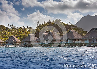 Island with palm trees and small houses on water in the ocean and mountains on a background Stock Photo