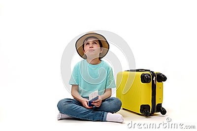Multi-ethnic teenage traveler boy in straw hat with suitcase and boarding pass, dreamily looking at copy space Stock Photo